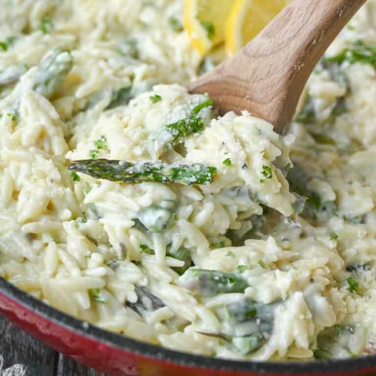 A wooden spoon scooping out some creamy orzo.