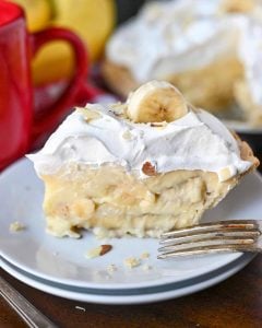 Slic of pie on a small white plate with a fork and red cup of coffee.