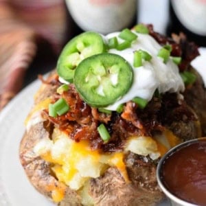 Pulled Pork Loaded Baked Potatoe on a white platoes with a side of BBQ sauce