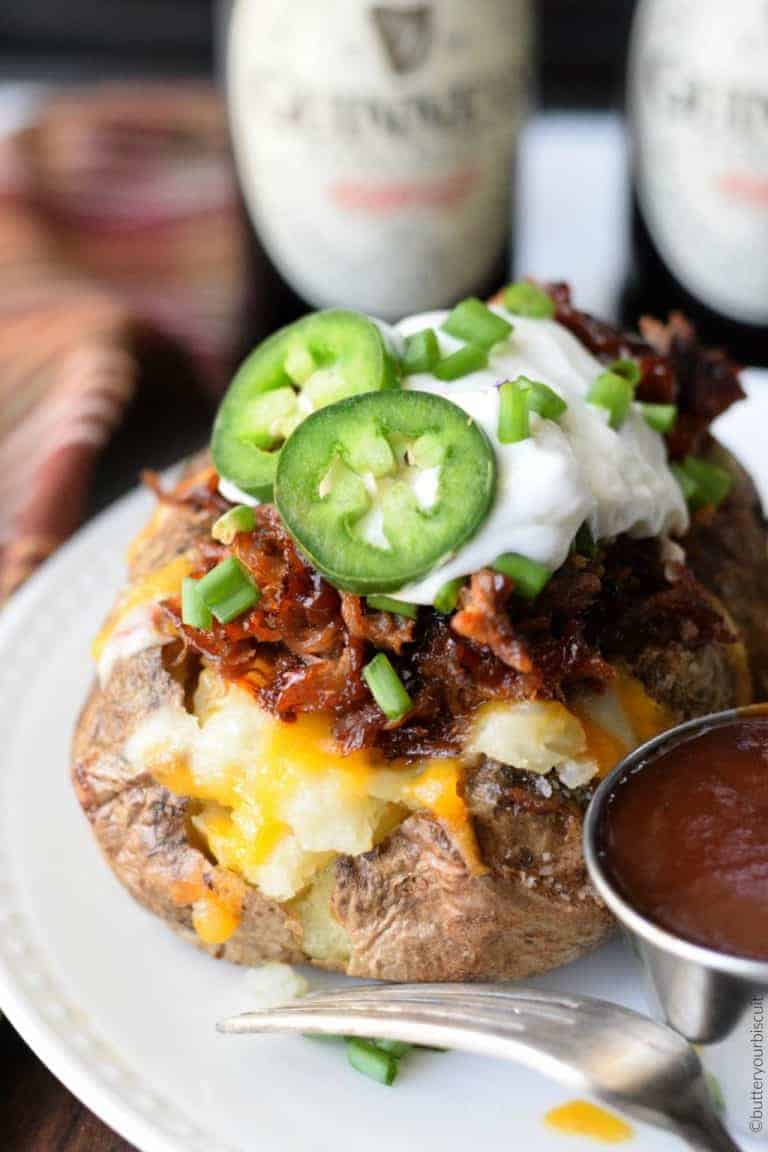 Pulled Pork Loaded Baked Potatoe on a white platoes with a side of BBQ sauce