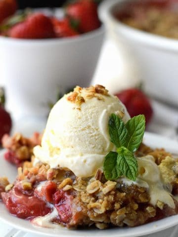 strawberry rhubarb pecan crisp on a white plate with a bowl of strawberries