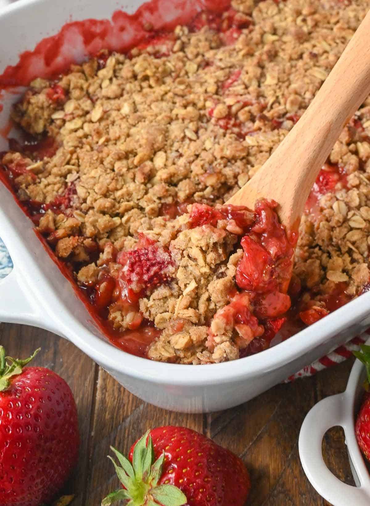 A wooden spoon scooping out a serving of strawberry crisp.