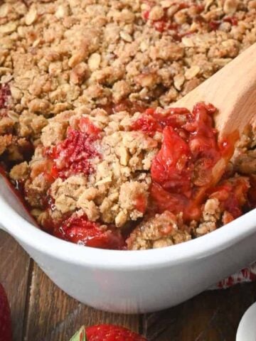 A wooden spoon scooping out a serving of strawberry crisp.