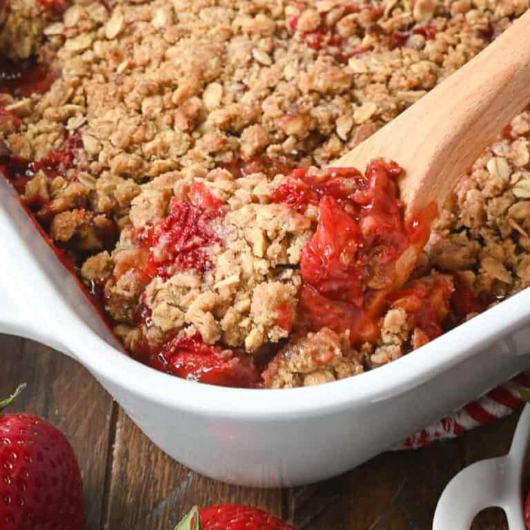 A wooden spoon scooping out a serving of strawberry crisp.