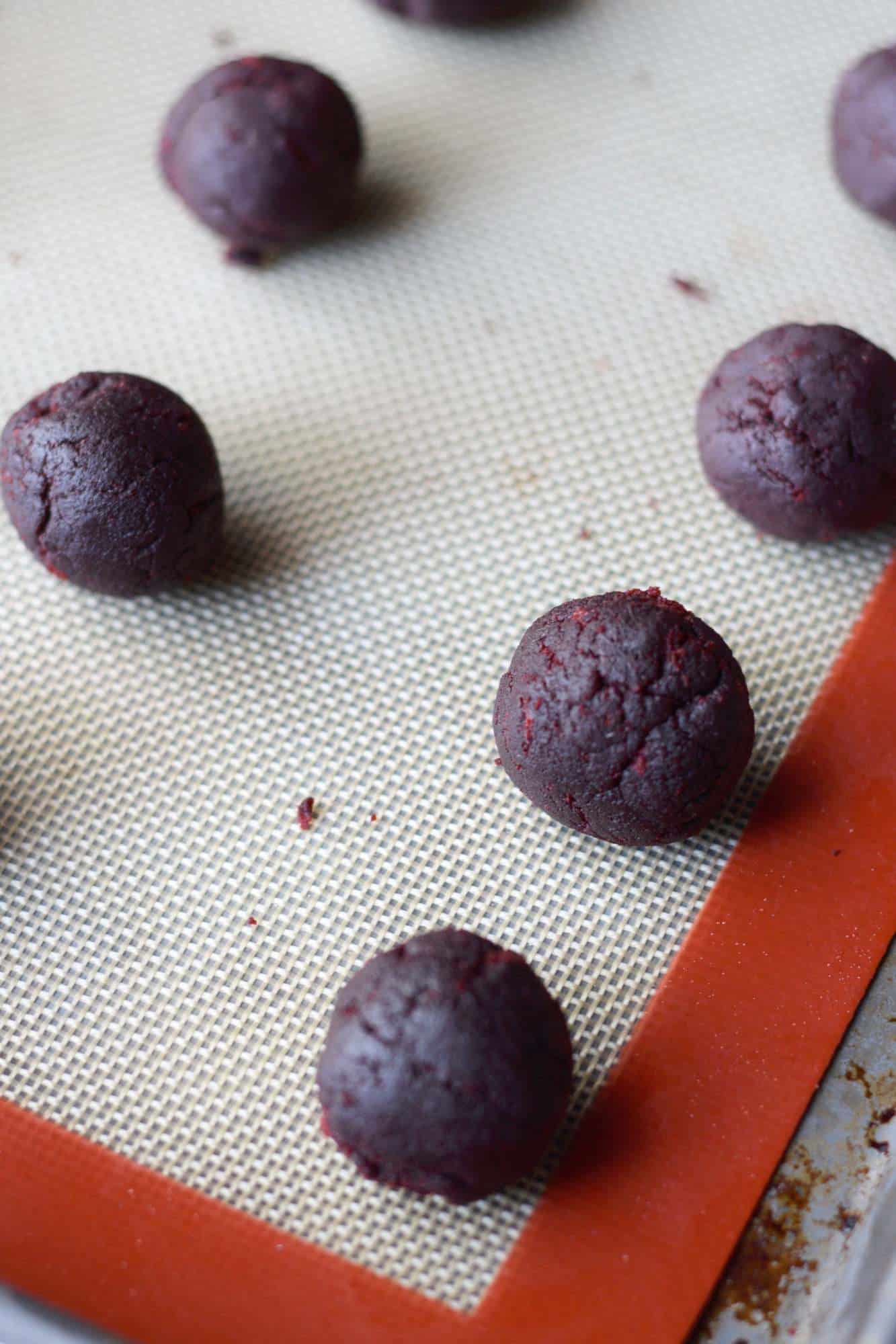 Red velvet cake balls on a baking sheet before being dipped in chocolate.