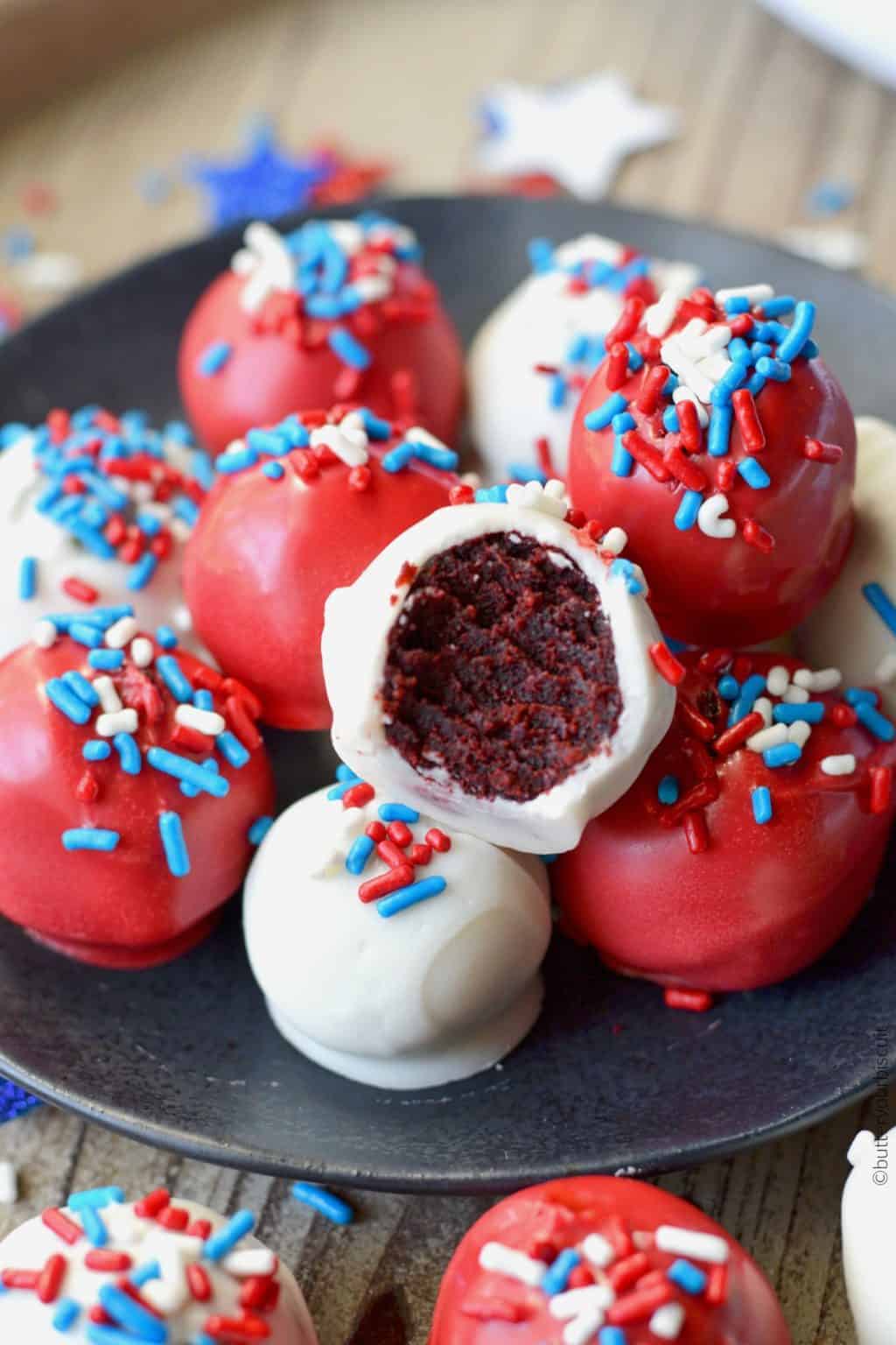 Patriotic Red Velvet Cake Balls all piled on a small black plate and one with a bite out of it.