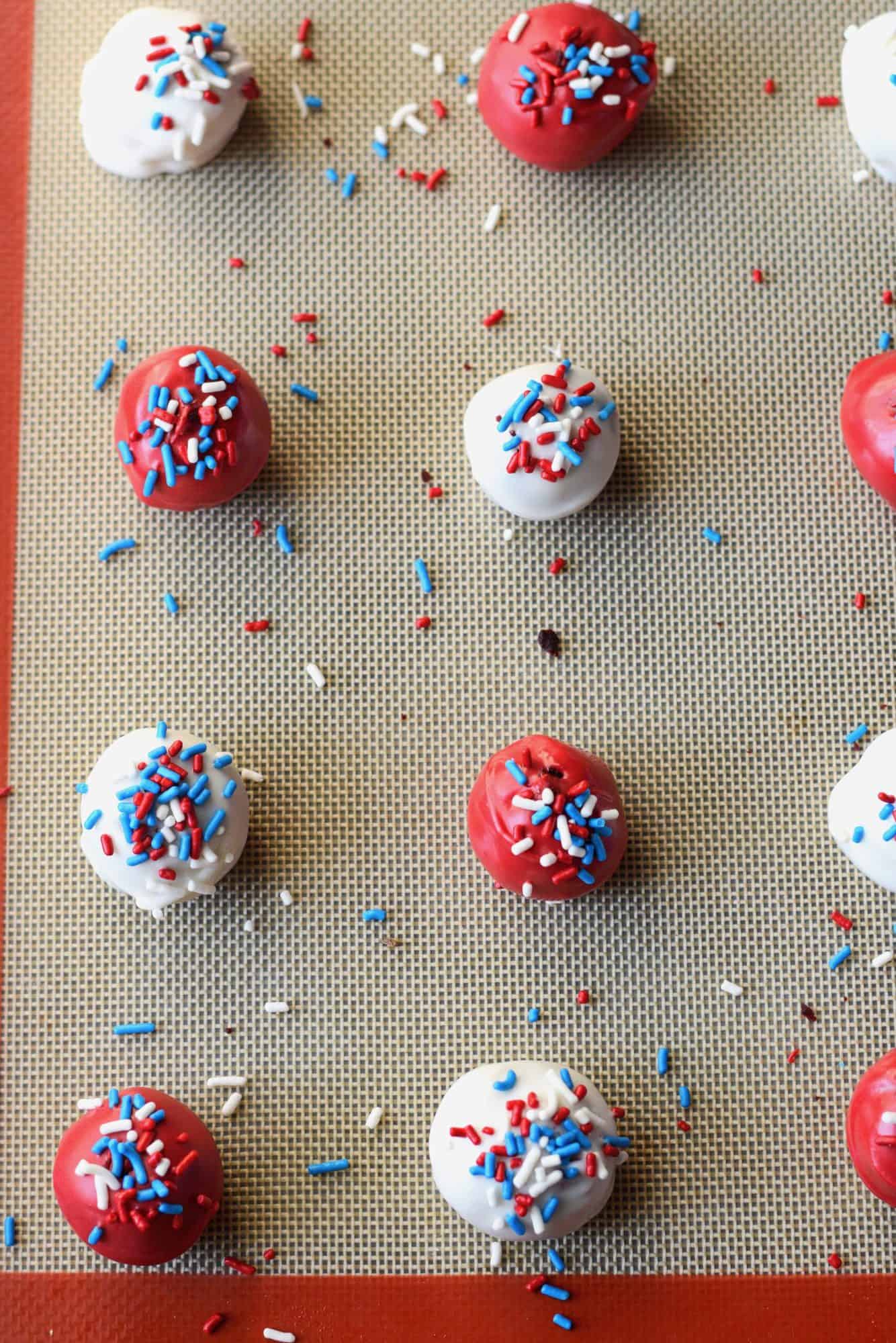 Cake balls dipped in white chocolate and red colored chocolate with festive sprinkles on top placed on a baking sheet to dry.
