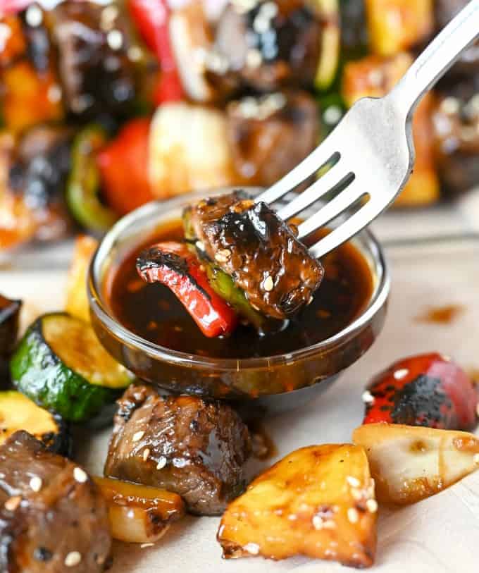 A bite of beef and zucchini on a fork being dipped into the leftover glaze.