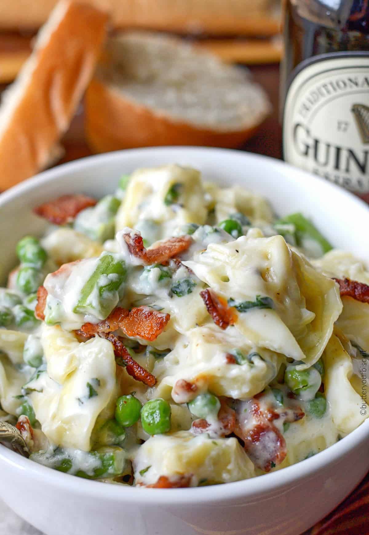 A bowl full of cheese tortellini and slices of bread on the side.