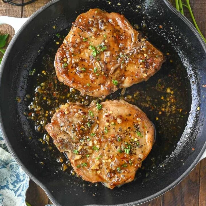 Two glazed pork chops in a cast iron skillet.