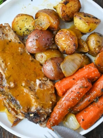 A slice of roasted pork on a plate with baby potatoes and roasted carrots.