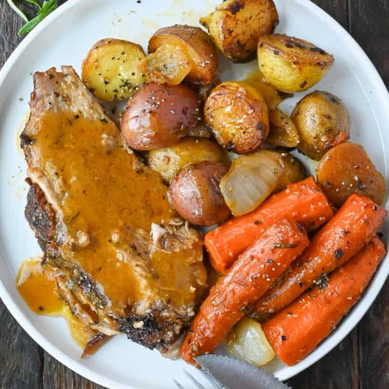 A slice of roasted pork on a plate with baby potatoes and roasted carrots.