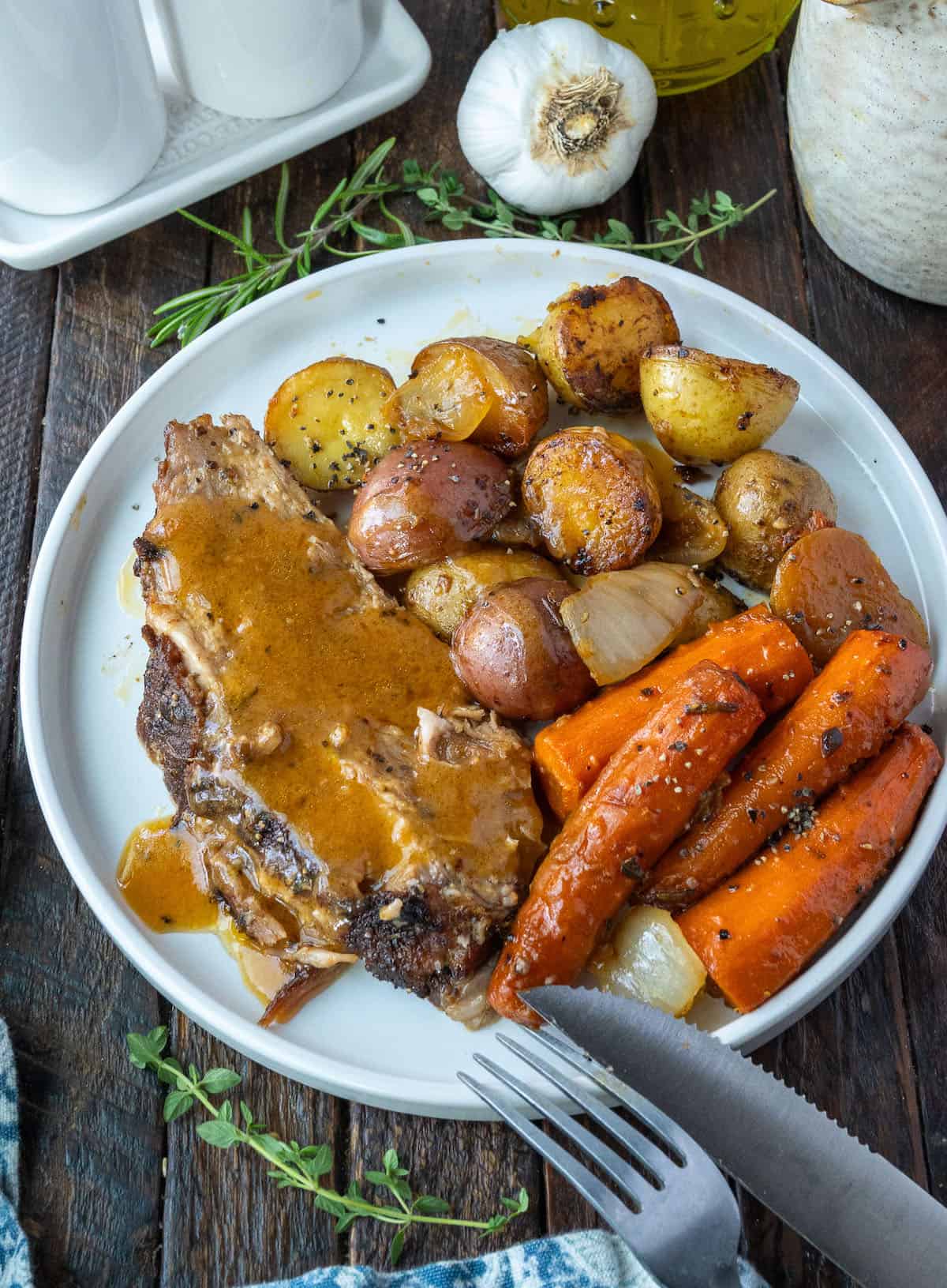 A slice of roasted pork on a plate with baby potatoes and roasted carrots.