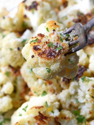 Parmesan roasted cauliflower in a white bowl with a fork grabbing one.