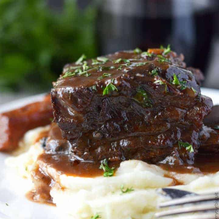 Beef short ribs braised in red wine on a plate with carrots and mashed potatoes