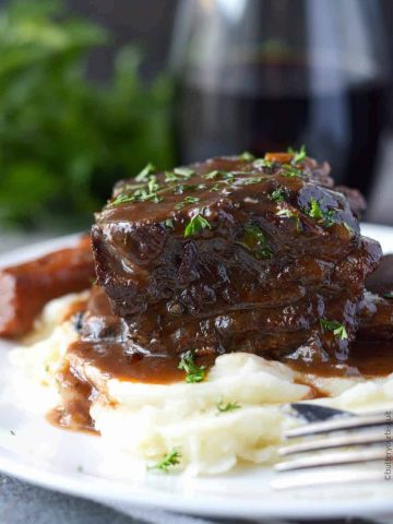 Beef short ribs braised in red wine on a plate with carrots and mashed potatoes