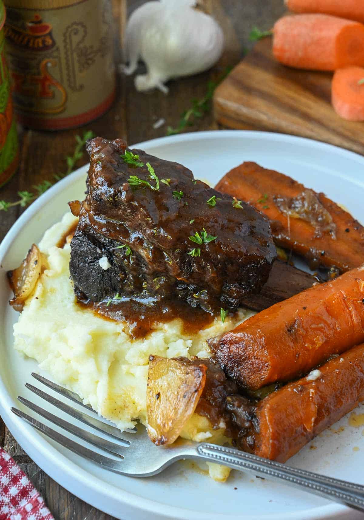 Wine braised short ribs with carrots and mashed potatoes on a plate.