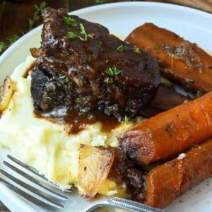 Wine braised short ribs with carrots and mashed potatoes on a plate.