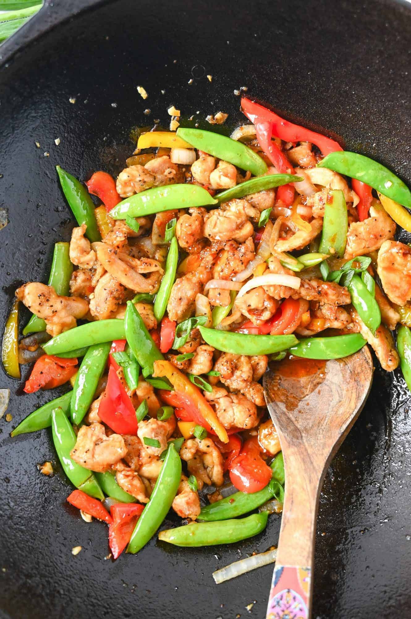 Sweet n spicy chicken stir fry in a cast iron wok and a wooden spoon.