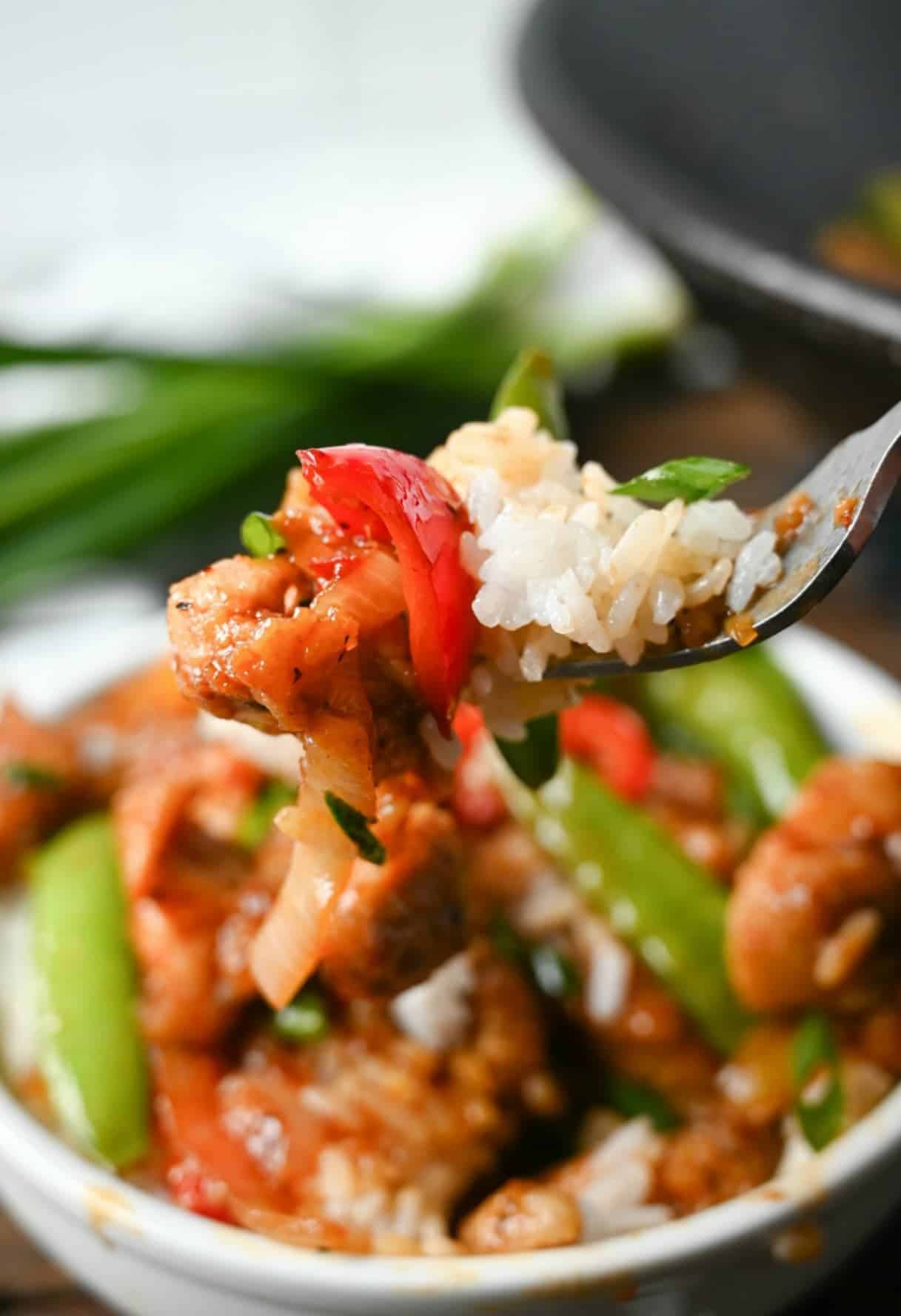 Chicken stir fry in a white bowl on top of white rice and a bite on a fork.
