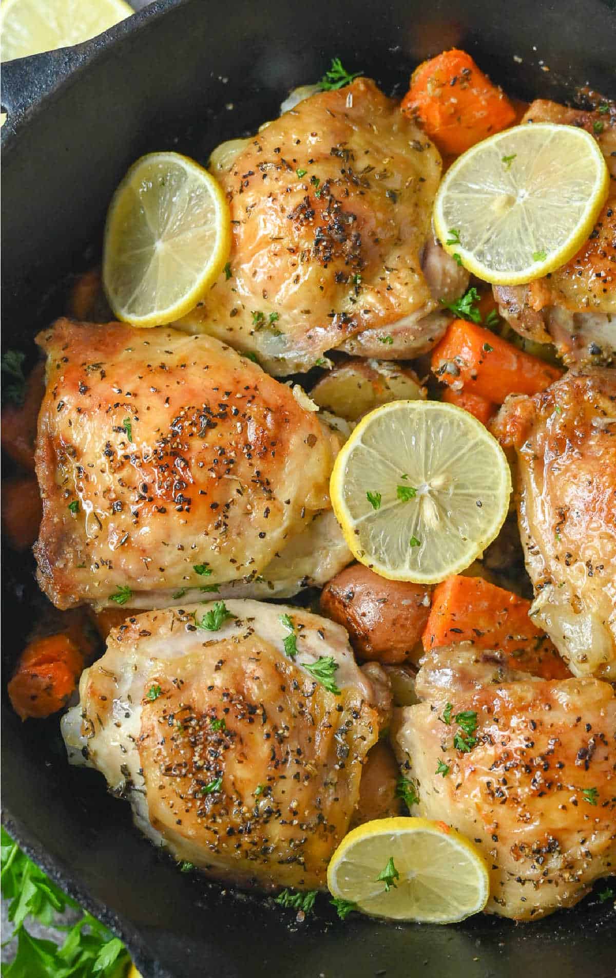 Chicken thighs roasted on top of potatoes and carrots in a pot.