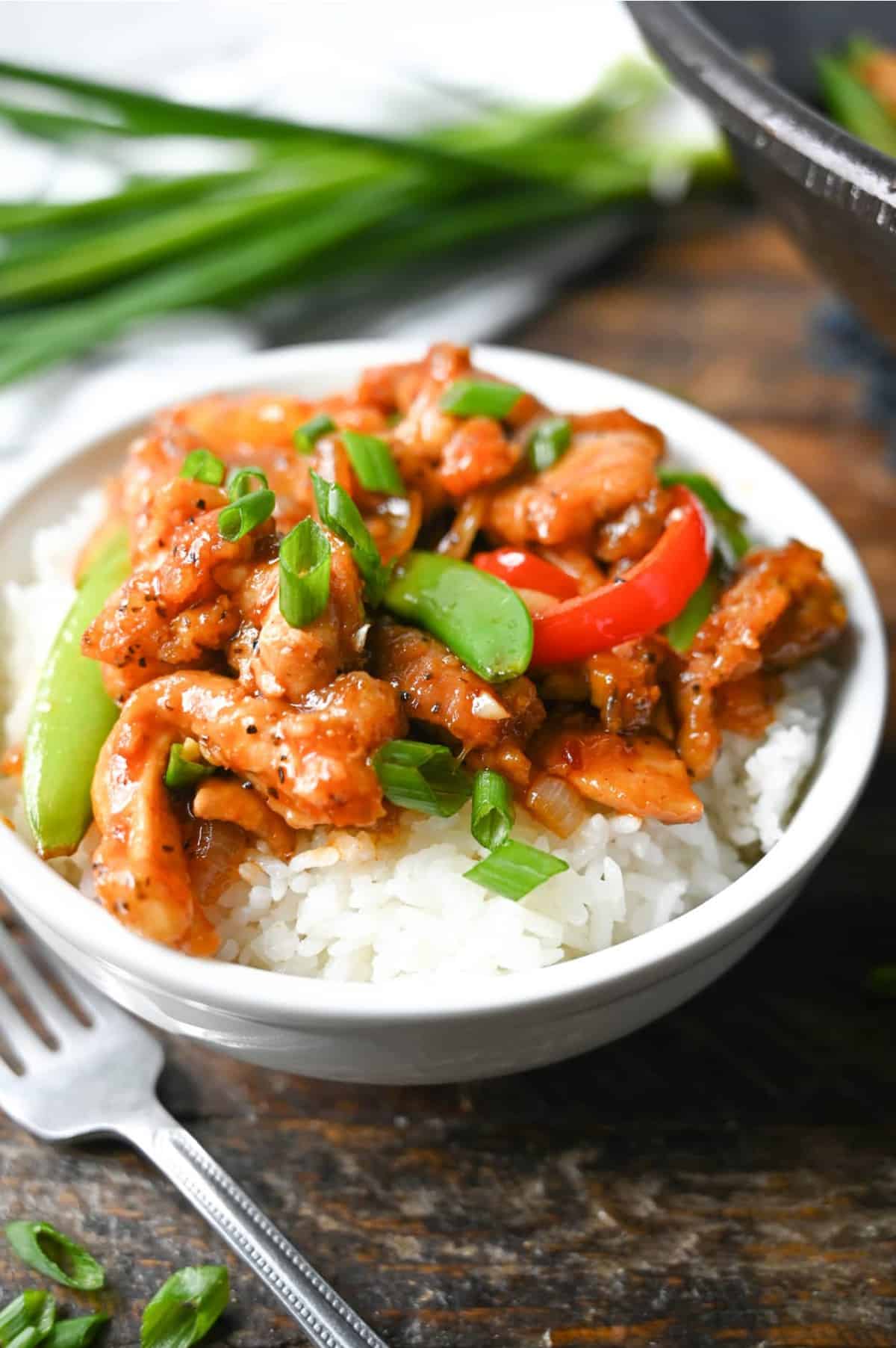 Sweet n spicy chicken stir fry piled on white rice in a white bowl.