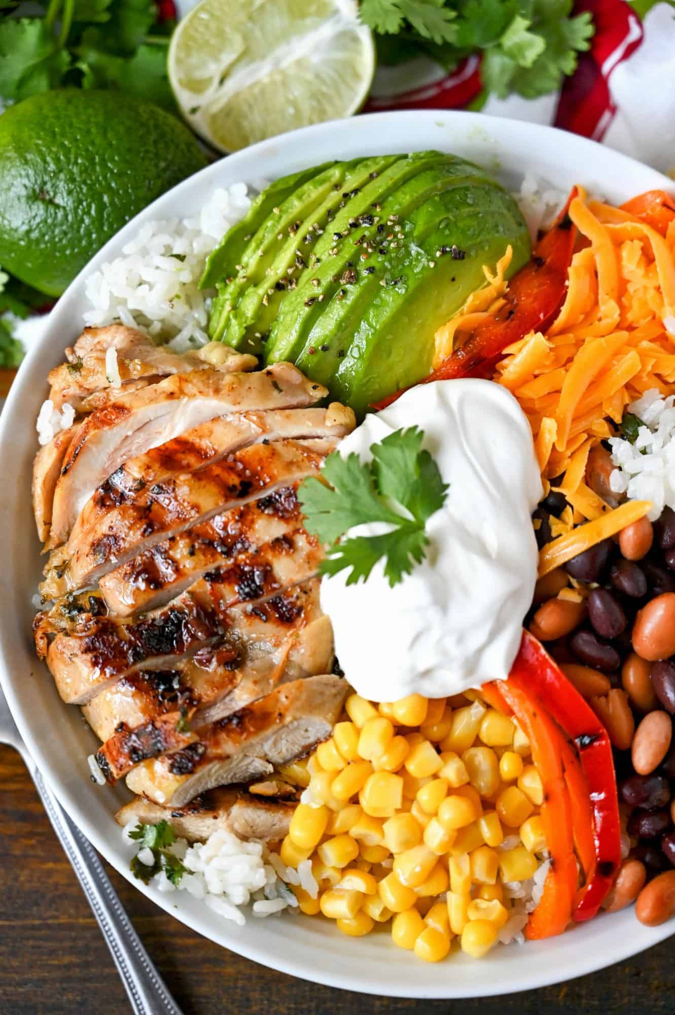 Tequila lime chicken, sliced avocado, scoop of corn, roasted red pepper slices, black beans. All piled on a bed of cilantro rice and a scoop of sour cream in a white bowl.