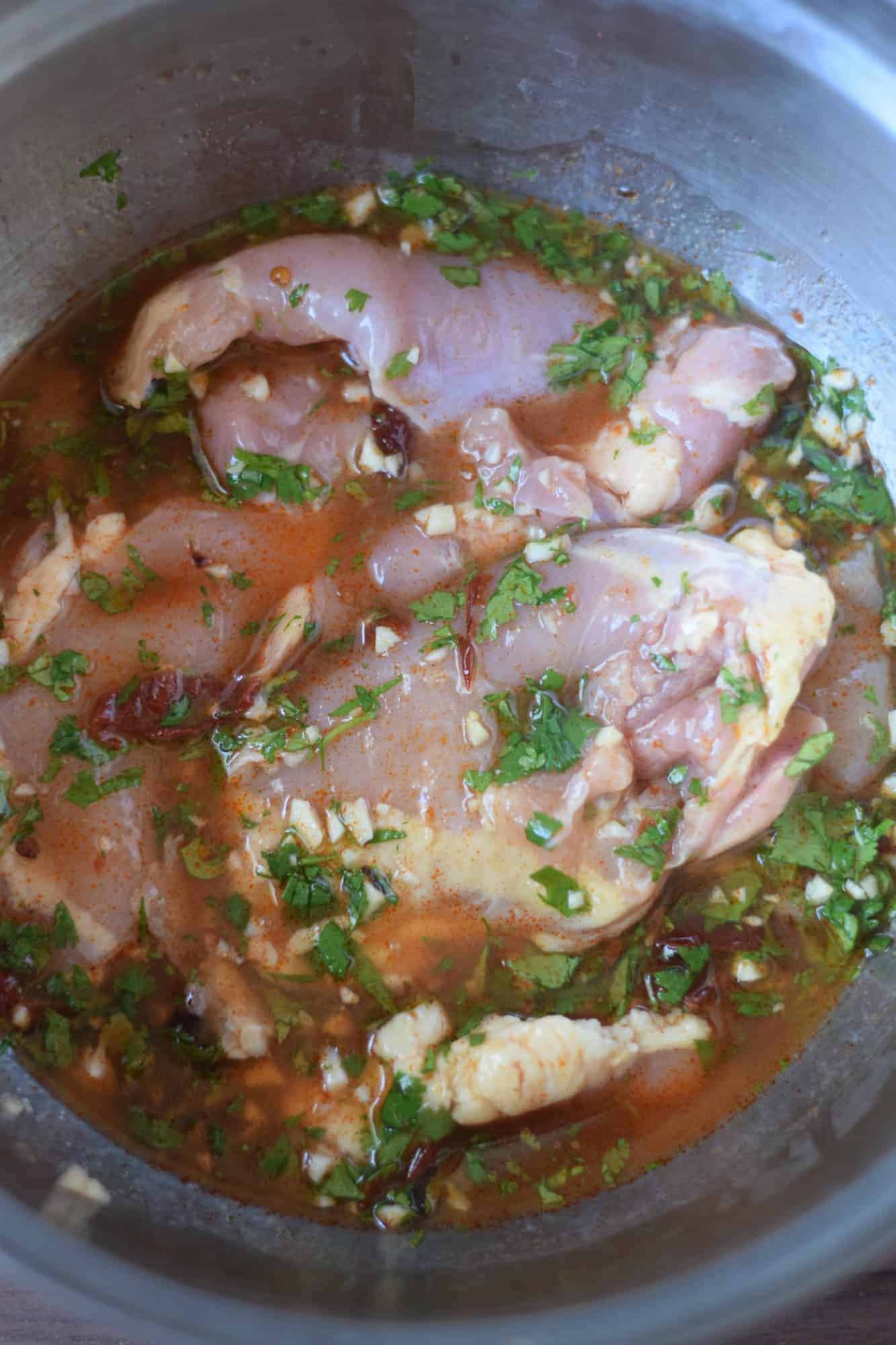 Chicken thighs marinading in a metal bowl.