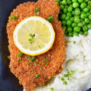Pork schnitzel with mashed potatoes and green peas on a black plate