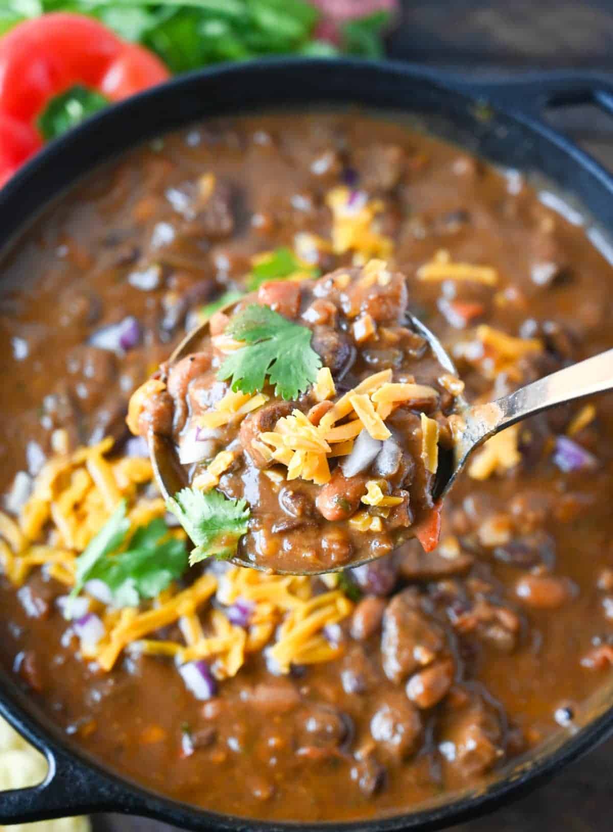 Steak chili in a large cast iron pot and a ladle scooping up a serving.