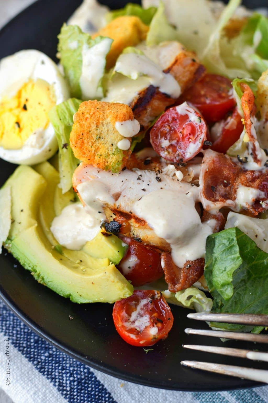 grilled chicken avocado salad on a black plate with a fork