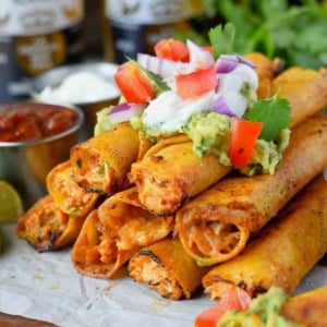 Chicken taquitos stacked with sour cream on top.