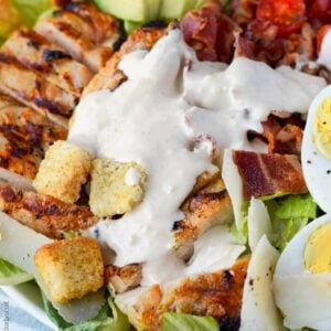 grilled chicken avocado caesar salad in a white bowl with caesar dressing