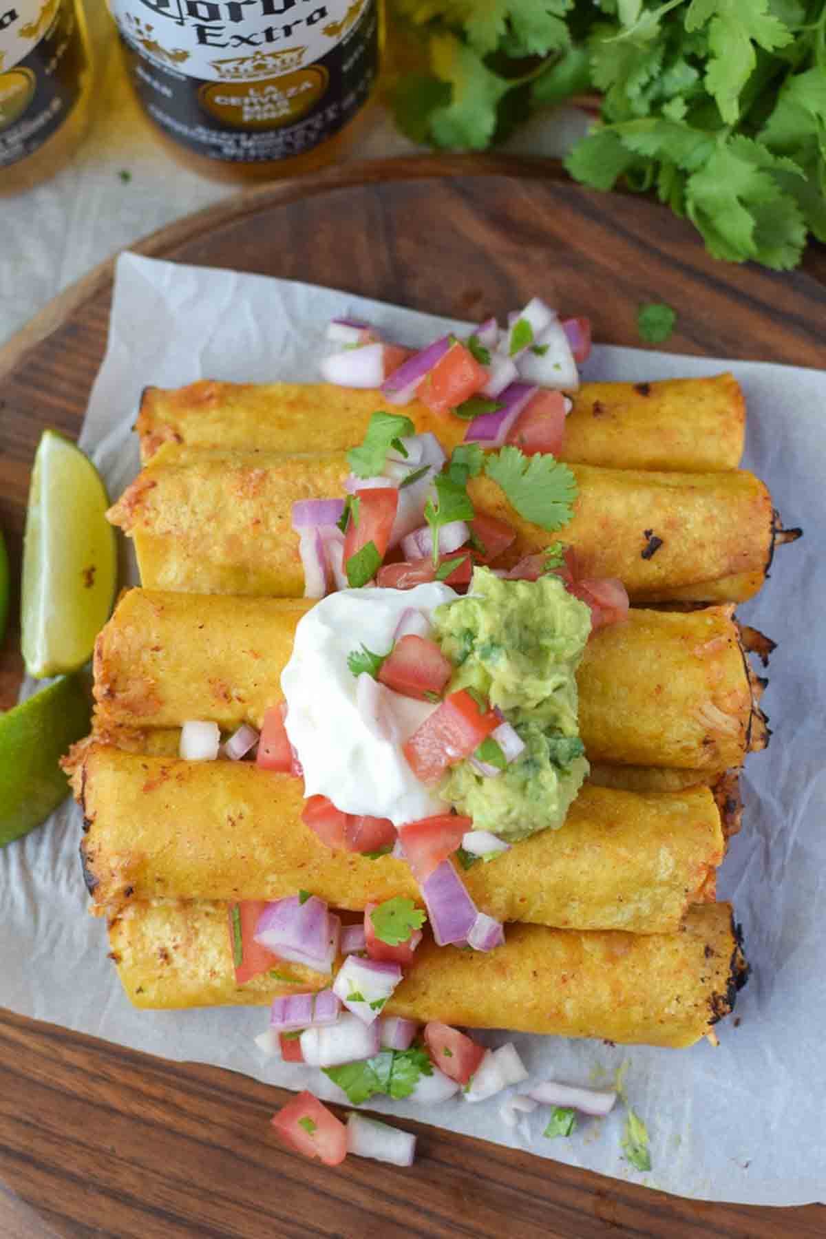 Chicken taquitos stacked with sour cream on top and limes on the side.
