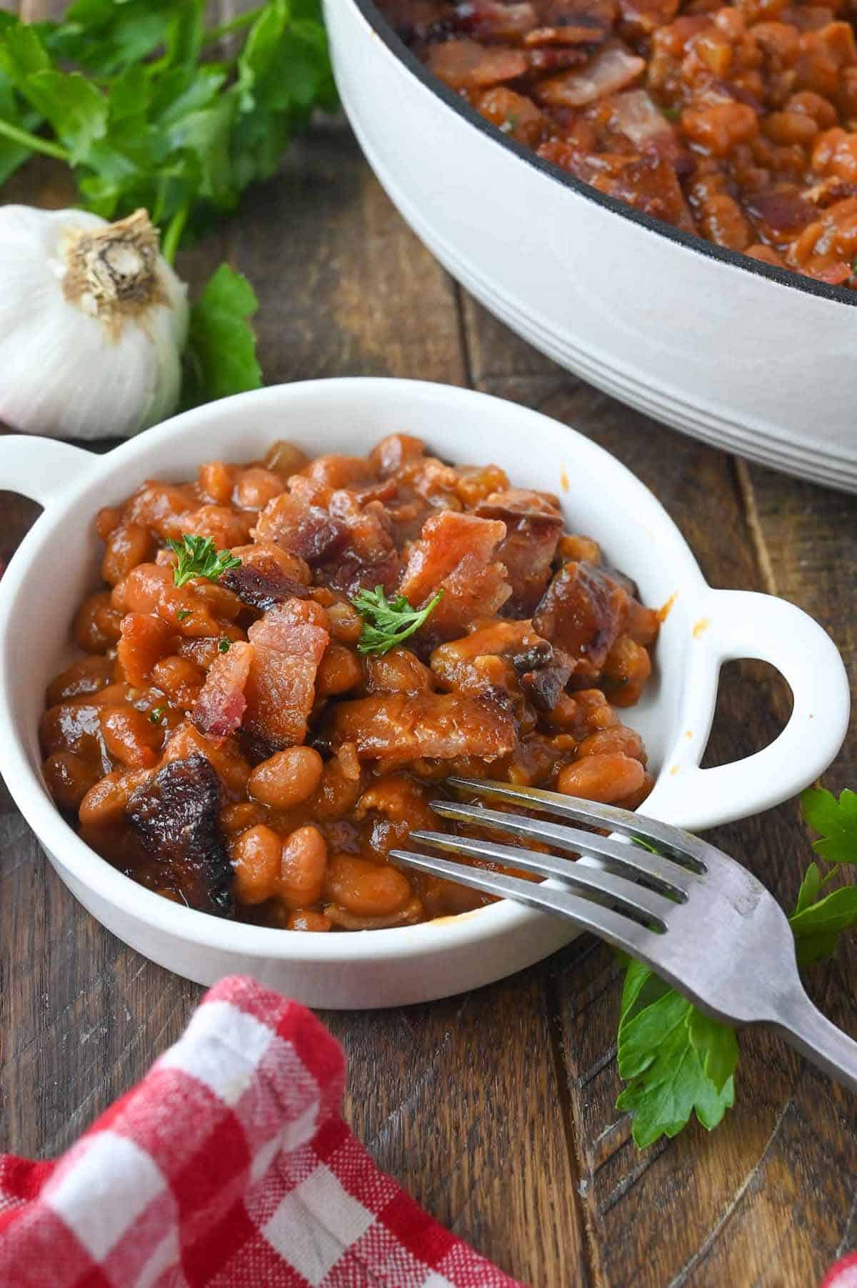 Baked beans in a small white dish with a fork.