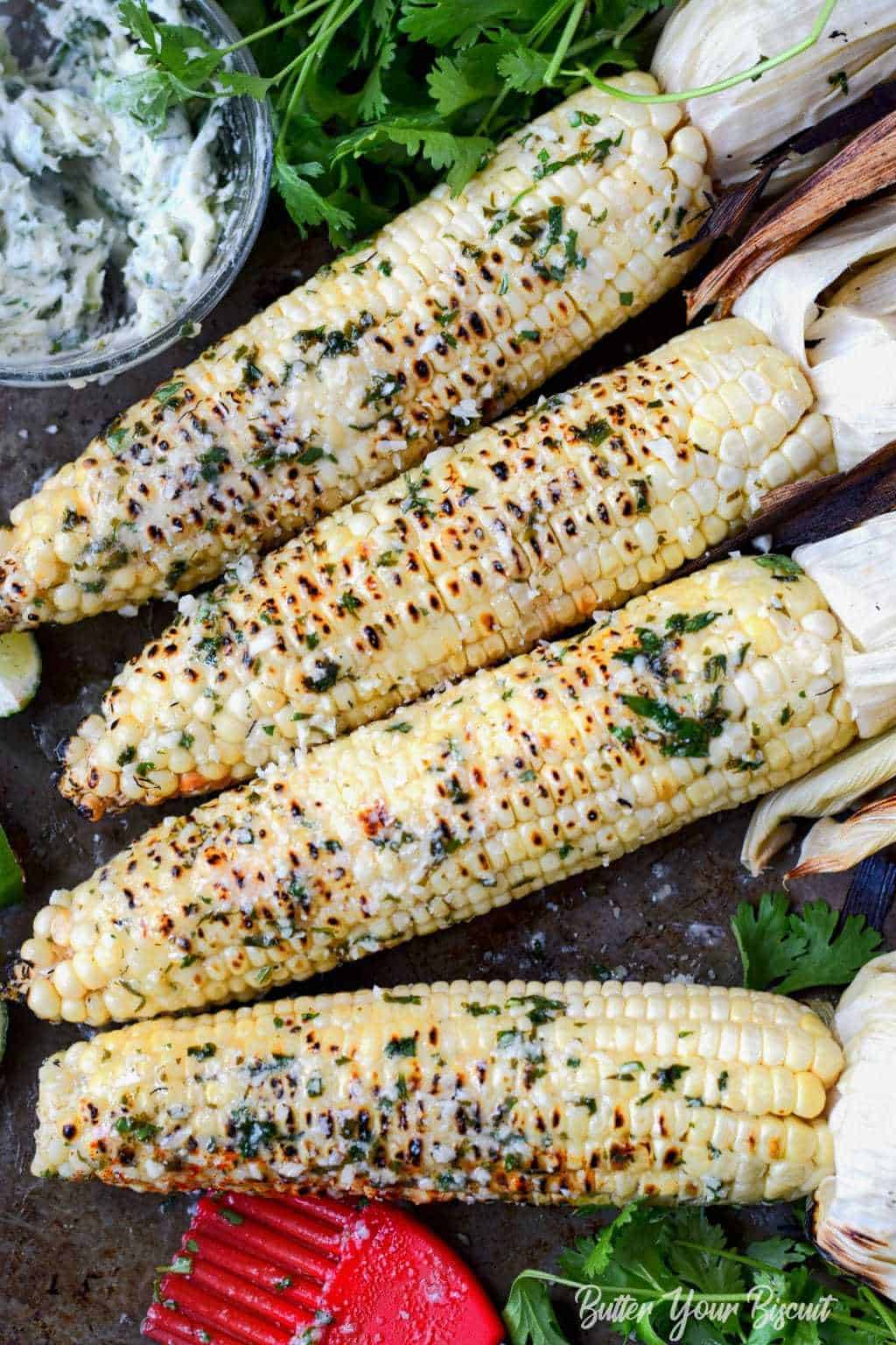 Four ears of grilled corn with cilantro lime butter spread on top.