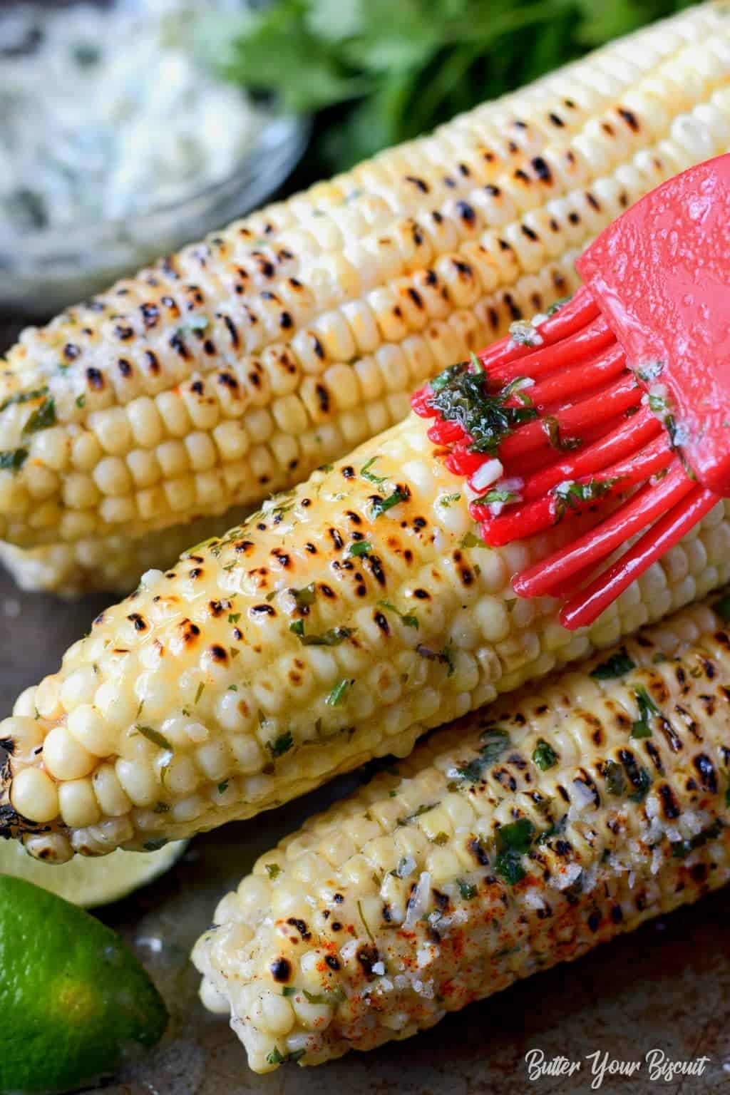 A close up photo of a red pastry brush brushing melted butter on top.