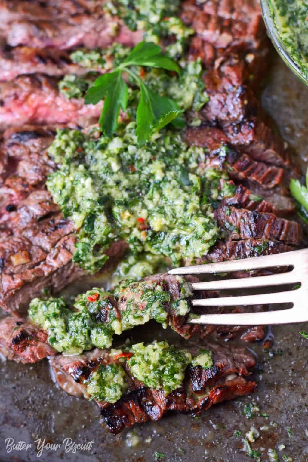 Grilled skirt steak and chimichurri on a baking sheet with a fork