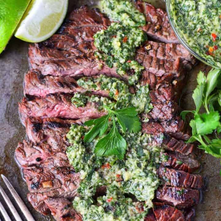 Grilled skirt steak and chimichurri spread on top with forks and lime slices