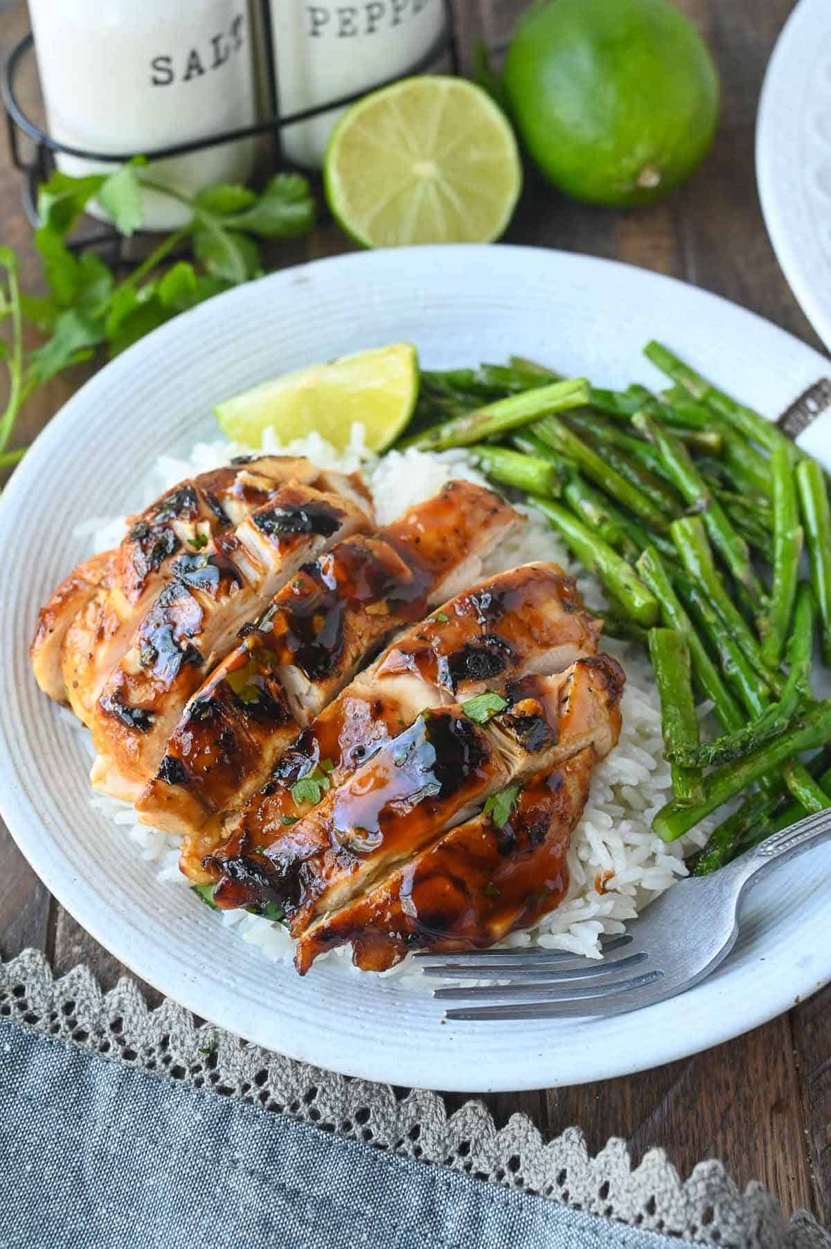 Sliced honey sriracha grilled chicken on a plate with coconut rice and asparagus.