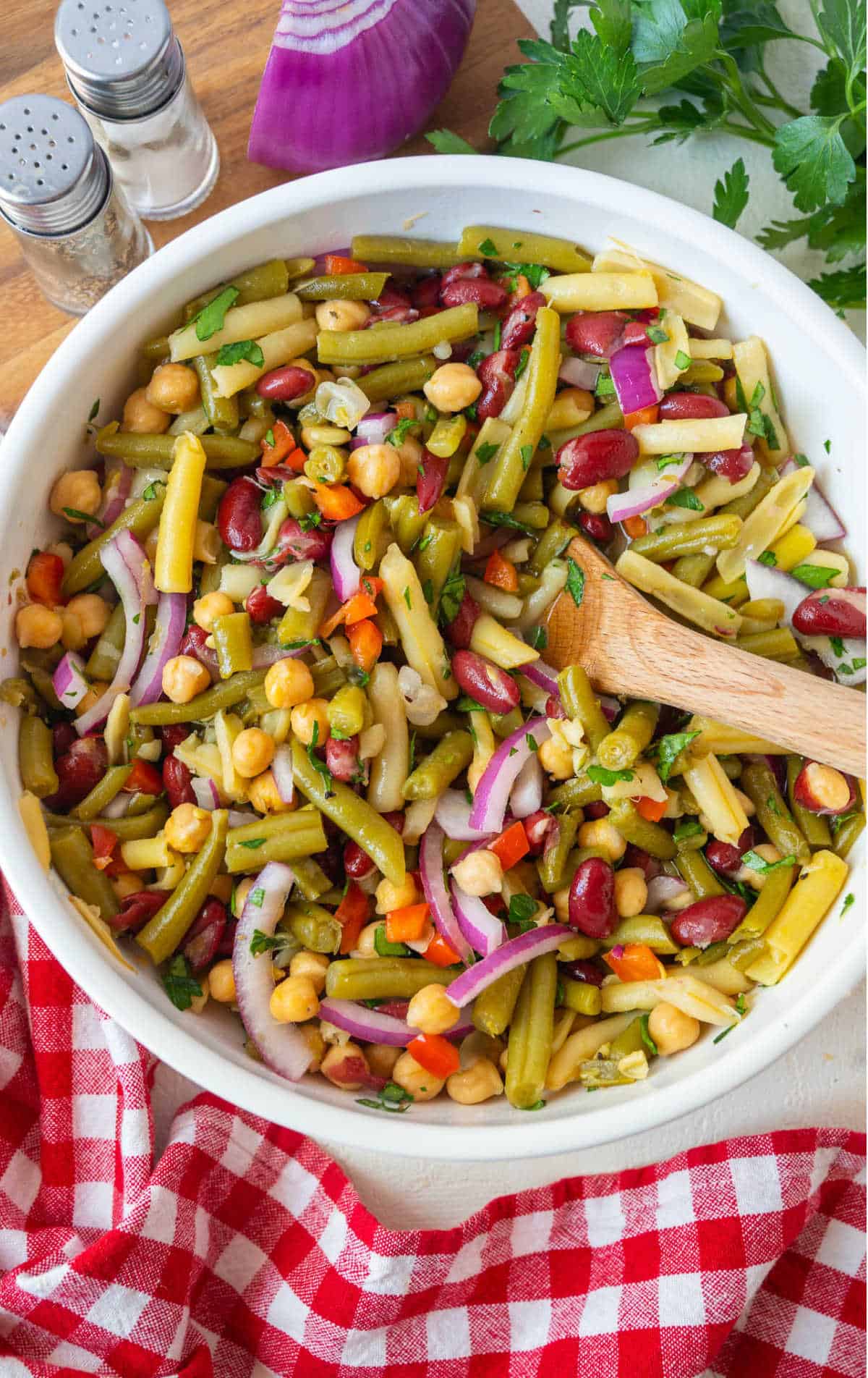 A large bowl of four bean salad with a wooden spoon.