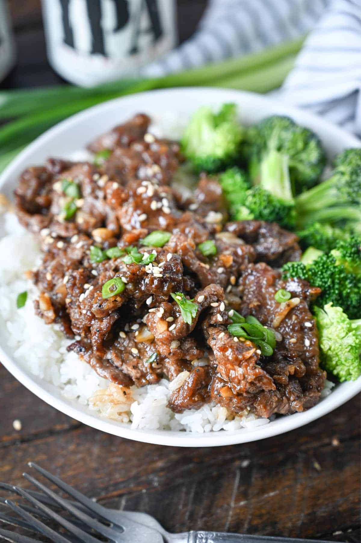 Mongolian beef on top of white rice with sesame seeds and green onions on top.