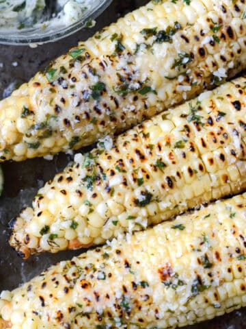A close up photo of three ears of corn that have been grilled with melted butter on top.