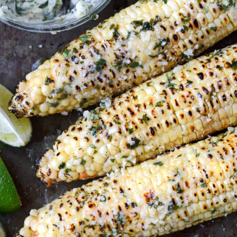 A close up photo of three ears of corn that have been grilled with melted butter on top.