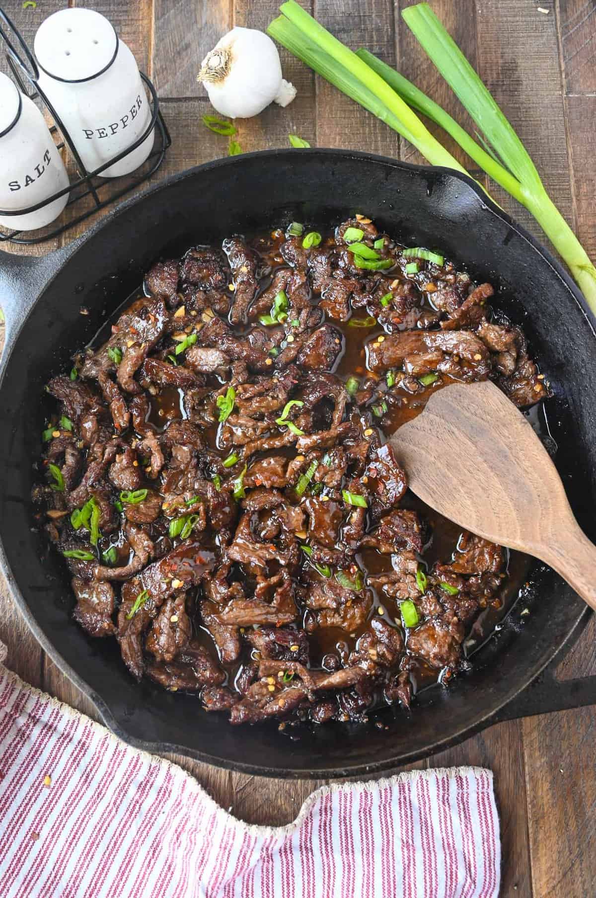 Mongolian beef in a cast iron skillet with sliced green onions on top.