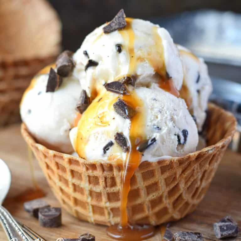 Three scoops of no churn caramel chocolate ice cream in a waffle bowl with extra caramel drizzled on top.