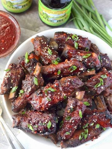 Chinese spare ribs piled on a whit plate with a side of sauce