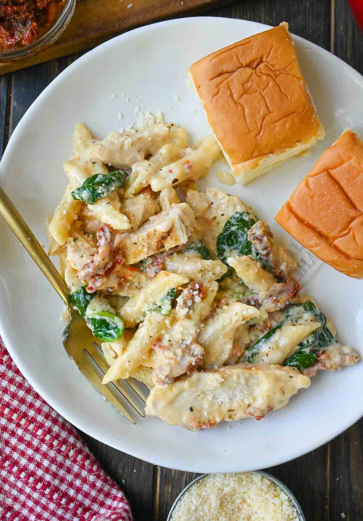 Chicken pasta on a plate with dinner rolls.