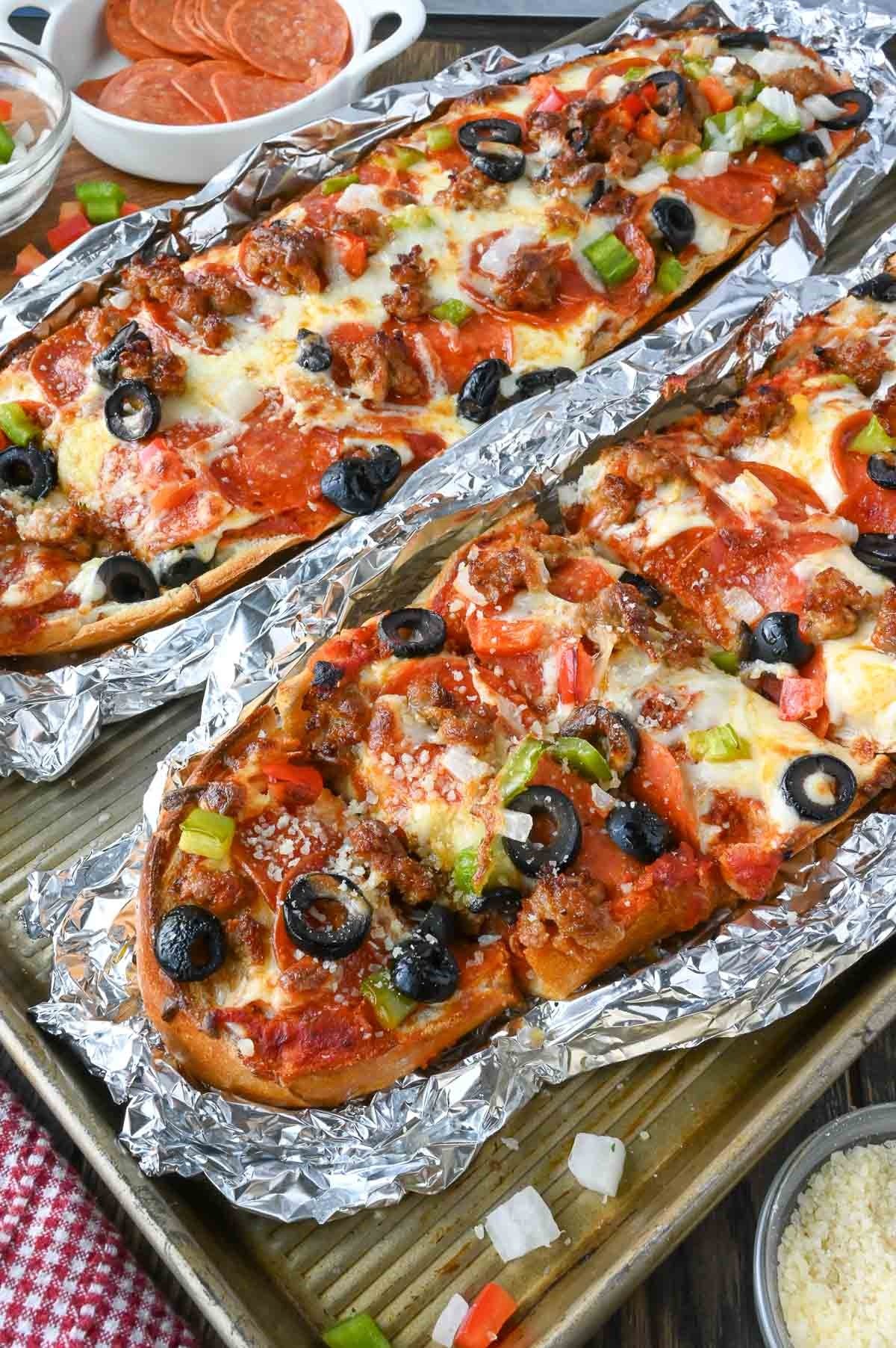 French bread pizza tucked into foil boats on a baking sheet.