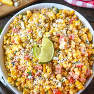Sweet corn salad in a large white bowl with corn on the cob on the side.